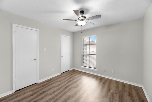 unfurnished bedroom with ceiling fan, wood finished floors, and baseboards