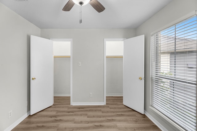 unfurnished bedroom with a walk in closet, baseboards, ceiling fan, and light wood-style floors