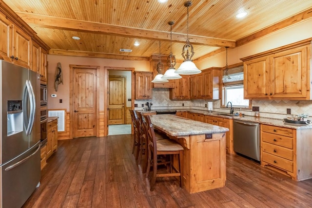 kitchen with beamed ceiling, a sink, appliances with stainless steel finishes, a kitchen island, and dark wood-style floors