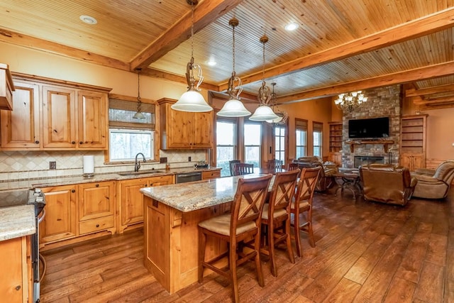 kitchen featuring beamed ceiling, appliances with stainless steel finishes, a sink, dark wood-style floors, and a center island
