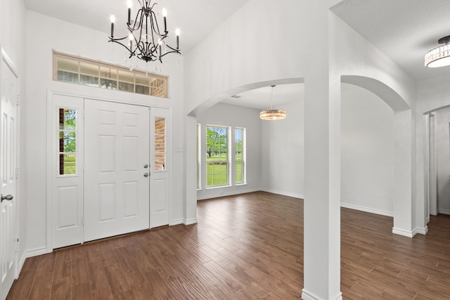 entrance foyer featuring arched walkways, wood finished floors, baseboards, a notable chandelier, and a towering ceiling
