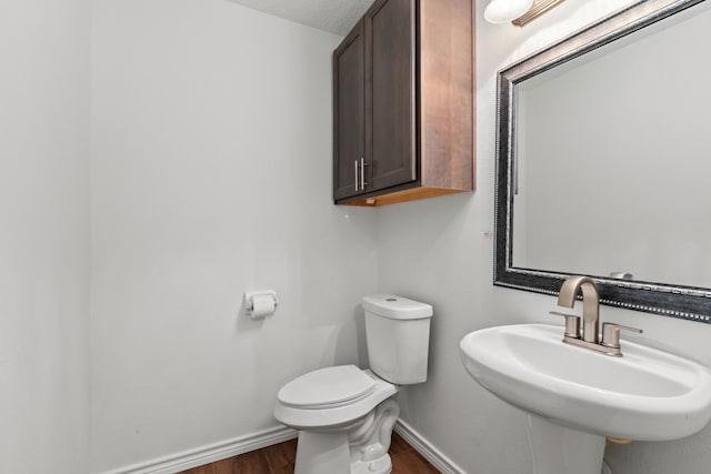 bathroom featuring wood finished floors, toilet, baseboards, and a sink