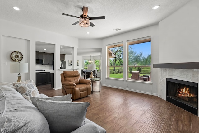 living room featuring dark wood finished floors, a premium fireplace, visible vents, a ceiling fan, and a textured ceiling