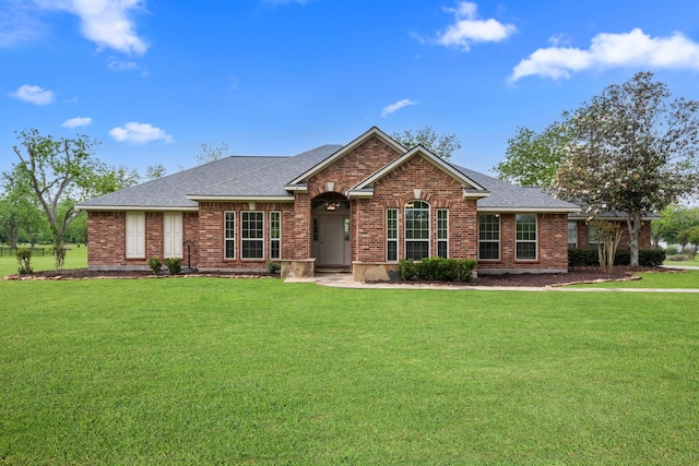 view of front of house with brick siding, a shingled roof, and a front yard