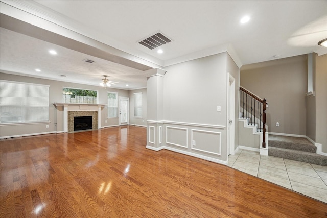 unfurnished living room with stairs, a tiled fireplace, ornamental molding, a ceiling fan, and recessed lighting