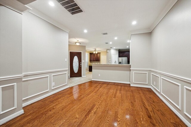 foyer entrance featuring a decorative wall, light wood-type flooring, recessed lighting, wainscoting, and crown molding