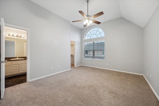 unfurnished bedroom with lofted ceiling, carpet flooring, a walk in closet, a sink, and ensuite bathroom
