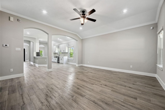 unfurnished living room with arched walkways, a ceiling fan, and crown molding