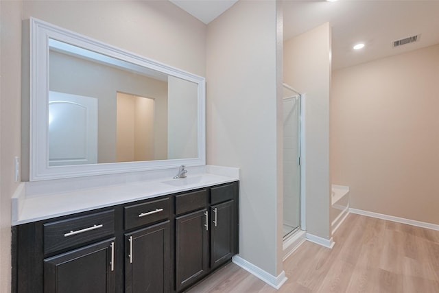 bathroom with wood finished floors, a shower stall, a bath, vanity, and visible vents