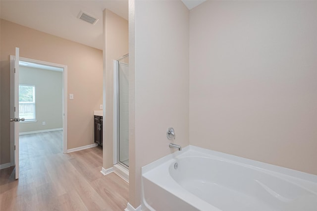 bathroom with wood finished floors, a shower stall, a bath, vanity, and visible vents