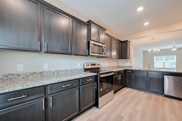 kitchen with light stone counters, a sink, appliances with stainless steel finishes, light wood-style floors, and a chandelier