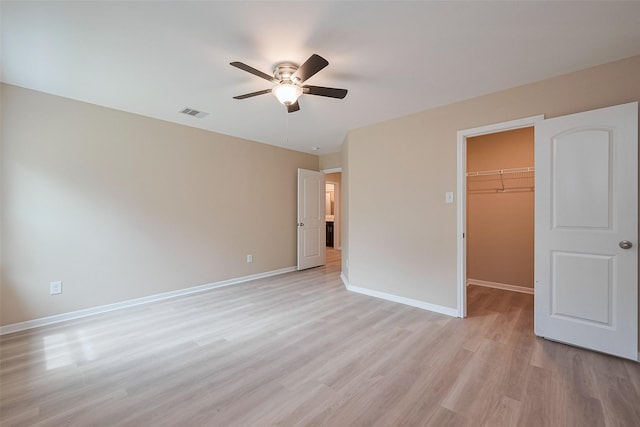 unfurnished bedroom with light wood finished floors, a closet, visible vents, baseboards, and a spacious closet