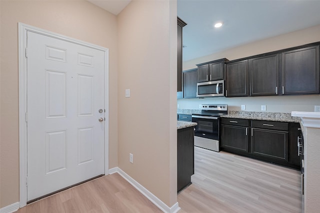 kitchen with appliances with stainless steel finishes, light wood-style floors, light stone countertops, and baseboards