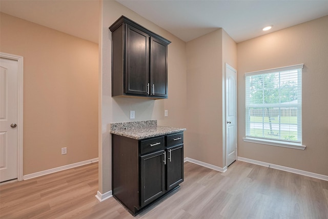 kitchen featuring light stone counters, dark brown cabinetry, light wood-style flooring, and baseboards
