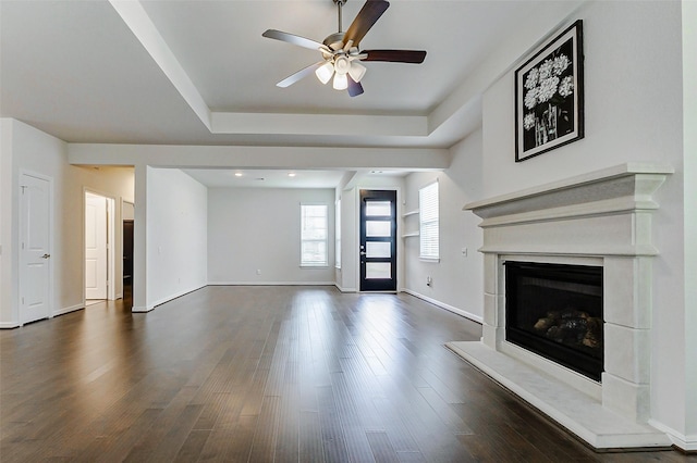 29031 Zacate Creek Ln, Fulshear, TX 77441 - unfurnished living room with ceiling fan, a raised ceiling, a fireplace with raised hearth, dark wood finished floors, and baseboards
