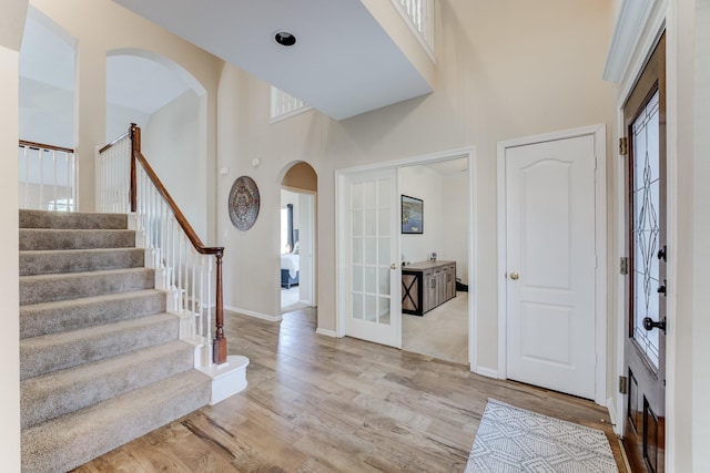 entrance foyer featuring light wood-style flooring, stairway, arched walkways, french doors, and a high ceiling