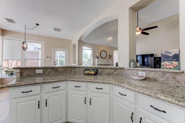 kitchen featuring arched walkways, visible vents, vaulted ceiling, and white cabinetry
