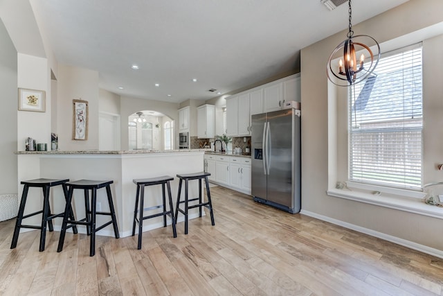 kitchen with a kitchen breakfast bar, white cabinetry, a chandelier, arched walkways, and stainless steel refrigerator with ice dispenser