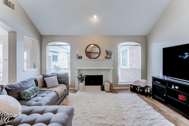 living area with lofted ceiling, a fireplace with flush hearth, visible vents, baseboards, and wood finished floors