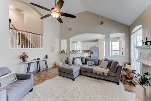 living area featuring arched walkways, visible vents, a ceiling fan, and wood finished floors