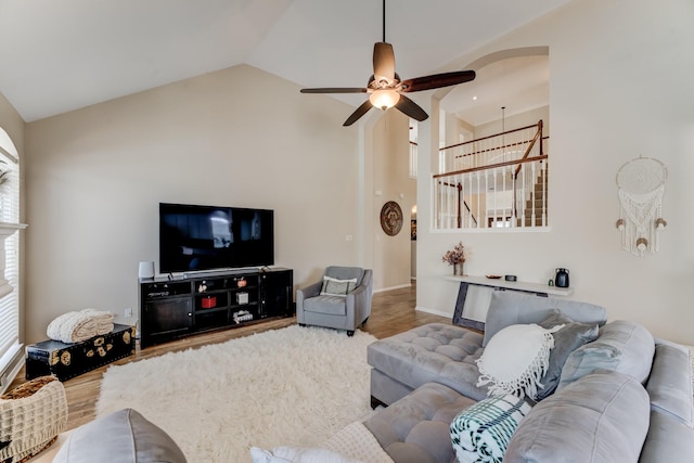 living room with ceiling fan, high vaulted ceiling, baseboards, arched walkways, and wood finished floors