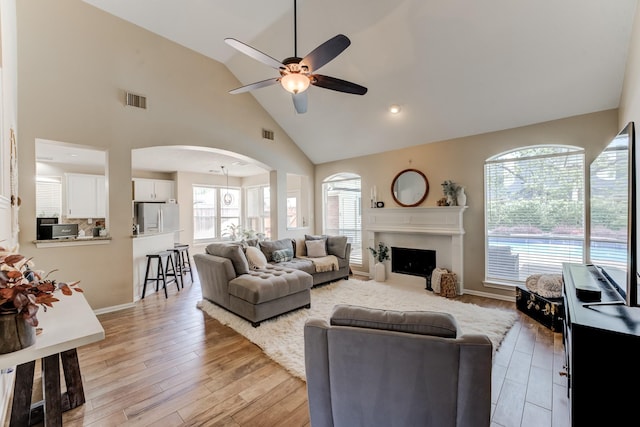living area with light wood finished floors, ceiling fan, high vaulted ceiling, visible vents, and arched walkways