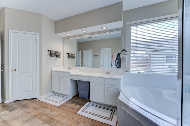 full bathroom with a bath, double vanity, a sink, and wood finished floors