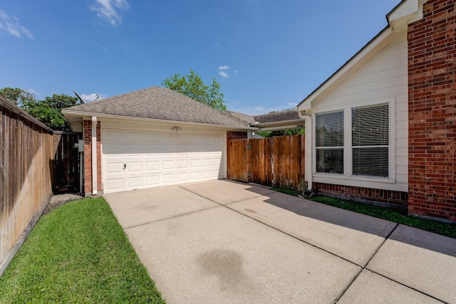 view of side of property featuring a garage, brick siding, fence, and roof with shingles