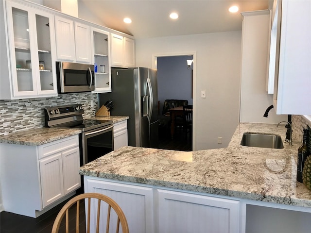 kitchen with stainless steel appliances, light stone counters, white cabinetry, and a sink