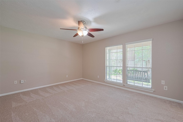 spare room featuring light colored carpet, a ceiling fan, and baseboards