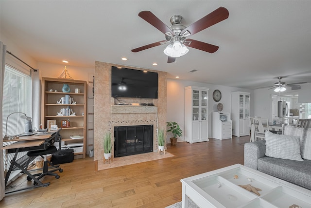living area featuring a tiled fireplace, a ceiling fan, and wood finished floors