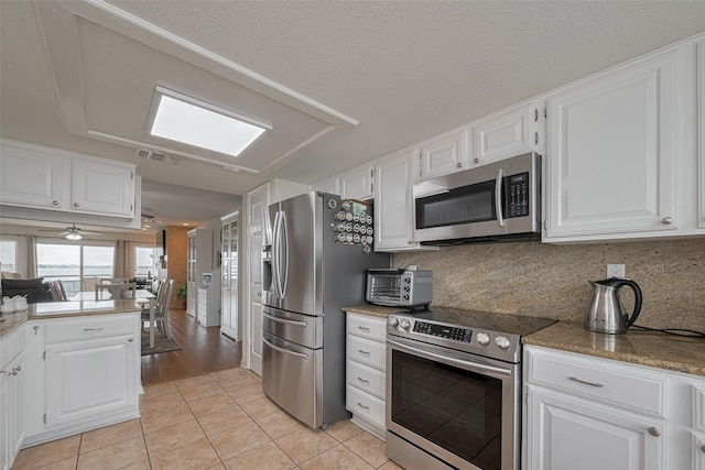kitchen with light tile patterned floors, stainless steel appliances, white cabinetry, and visible vents