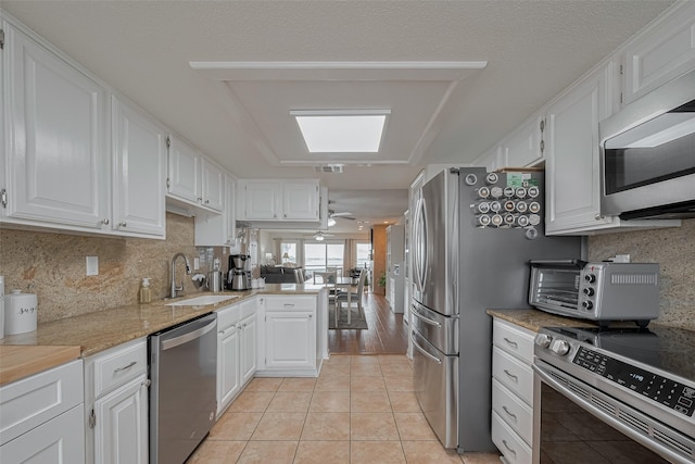kitchen with white cabinets, a sink, stainless steel appliances, a peninsula, and light tile patterned floors