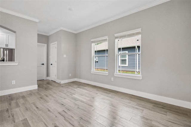 empty room with crown molding, light wood finished floors, and baseboards