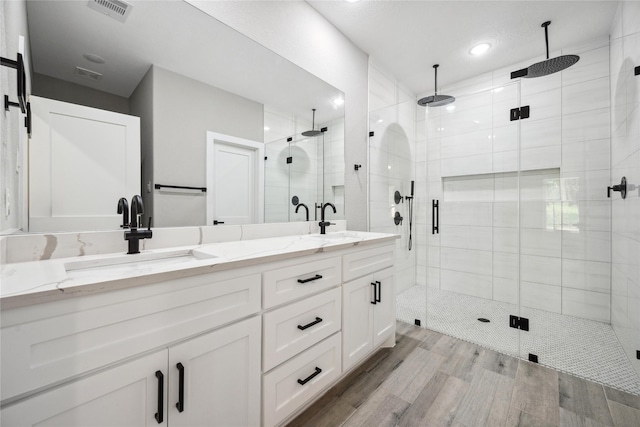 bathroom featuring a shower stall, a sink, double vanity, visible vents, and wood finished floors