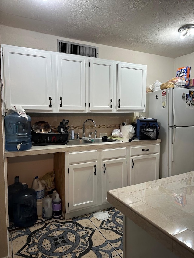 16203 Rapidcreek Dr, Houston, TX 77053 - kitchen with freestanding refrigerator, a sink, white cabinets, a textured ceiling, and tile counters