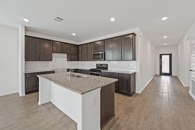 kitchen with a kitchen island with sink, a sink, appliances with stainless steel finishes, visible vents, and dark brown cabinets