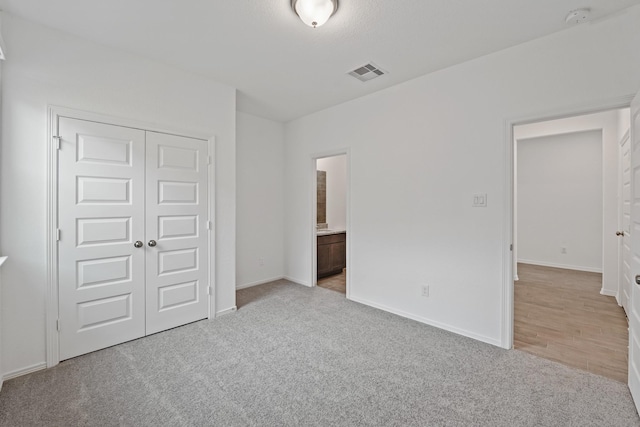 unfurnished bedroom featuring carpet floors, a closet, ensuite bathroom, baseboards, and visible vents