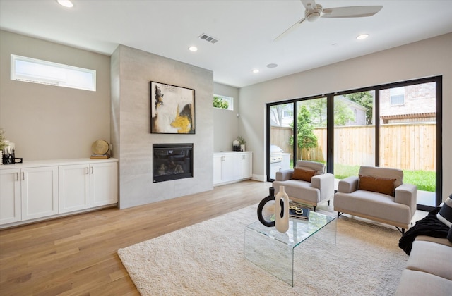 living area featuring visible vents, a ceiling fan, light wood-type flooring, and a fireplace