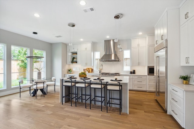 kitchen featuring a breakfast bar area, built in refrigerator, visible vents, light countertops, and wall chimney exhaust hood