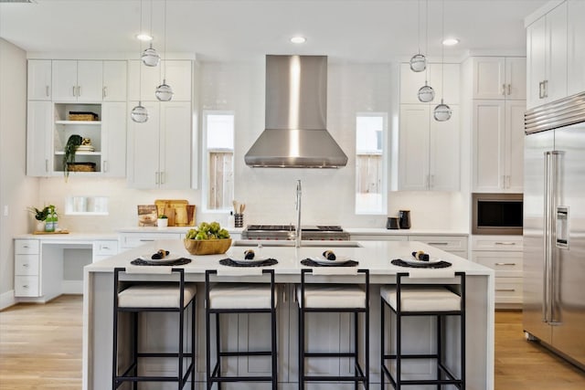 kitchen featuring recessed lighting, light countertops, wall chimney range hood, stainless steel built in refrigerator, and white cabinetry