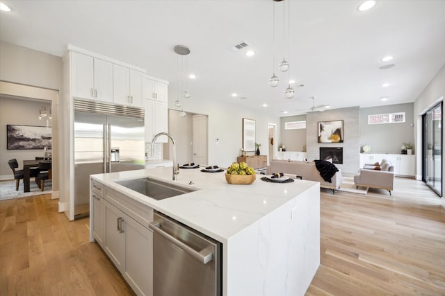 kitchen featuring a kitchen island with sink, stainless steel appliances, light wood-style floors, a sink, and visible vents