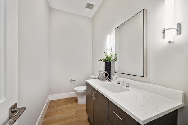 bathroom with wood finished floors, toilet, vanity, baseboards, and visible vents