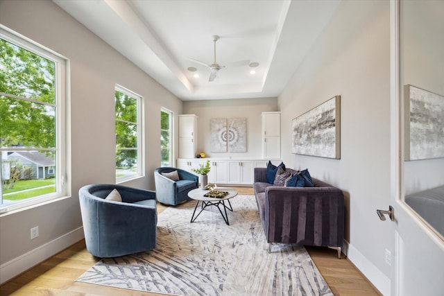 living area with a tray ceiling, ceiling fan, baseboards, and light wood-style floors