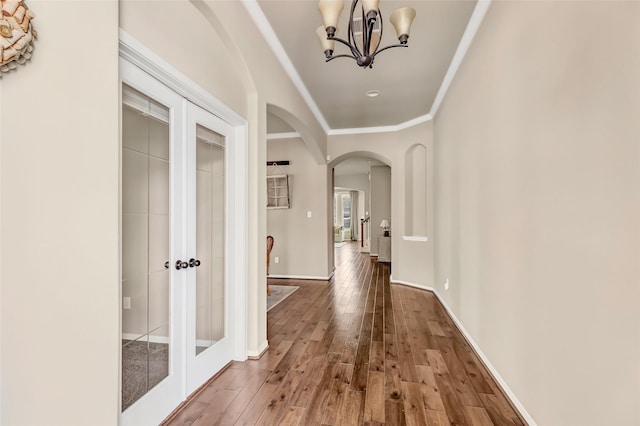 corridor with an inviting chandelier, arched walkways, crown molding, baseboards, and hardwood / wood-style flooring