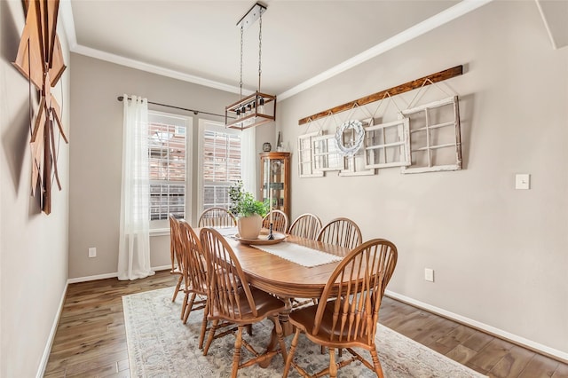 dining space featuring wood finished floors, crown molding, and baseboards