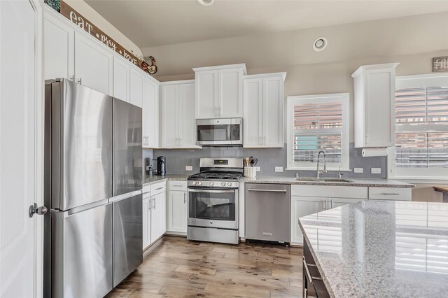 kitchen with stainless steel appliances, a sink, light stone countertops, tasteful backsplash, and white cabinetry