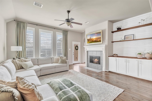 living room featuring visible vents, a tiled fireplace, a ceiling fan, and light wood-style flooring