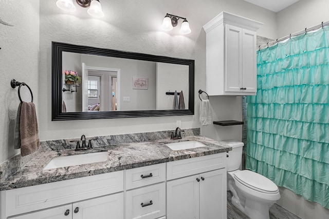 bathroom with a textured wall, toilet, double vanity, and a sink