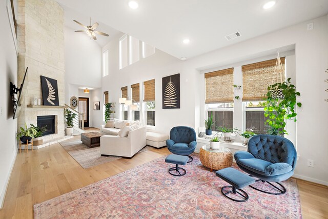 living area featuring a fireplace, a ceiling fan, baseboards, wood finished floors, and visible vents